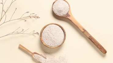 Colheres e tigela de madeira com fibras naturais em pó, representando alimentos ricos em fibras para o bom funcionamento do intestino.
