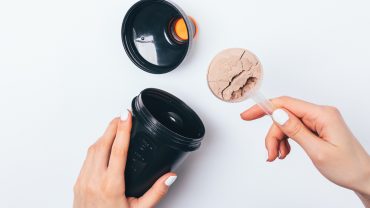 Mãos de uma mulher colocando um scoop de proteína na shakeira