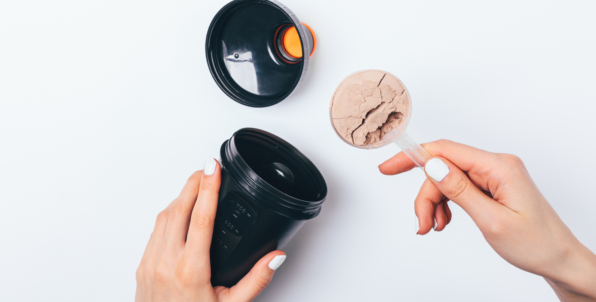 Mãos de uma mulher colocando um scoop de proteína na shakeira