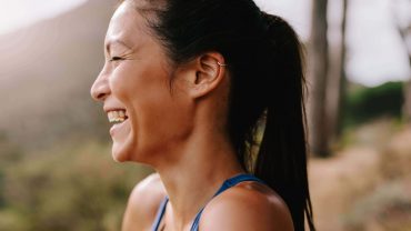 Mulher corredora sorri. Ela está de perfil com roupas esportivas pela manhã.