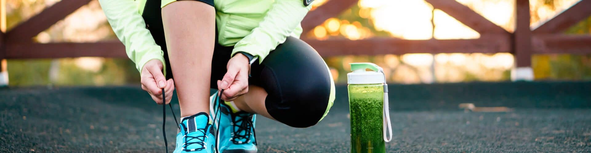 Atleta amarrando o tênis com um shake de receitas pré-treino ao lado