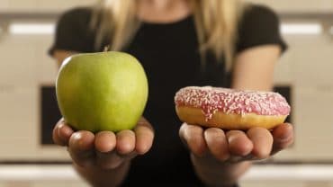 mulher compara uma maçã com um doce, um em cada mão