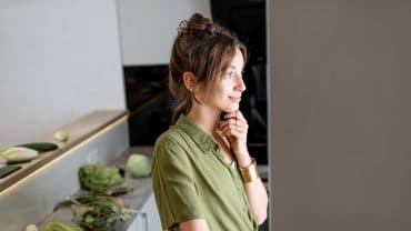 Mulher de perfil, olhando para a geladeira aberta na cozinha de casa.