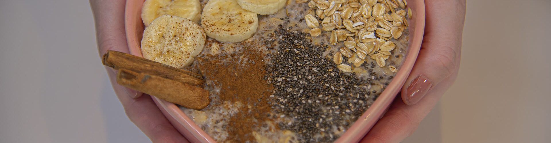 Mãos segurando bowl em forma de coração com mingau de aveia com banana