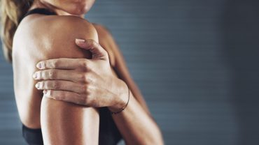 mulher de perfil segurando o braço, fazendo menção a dor e inflamação