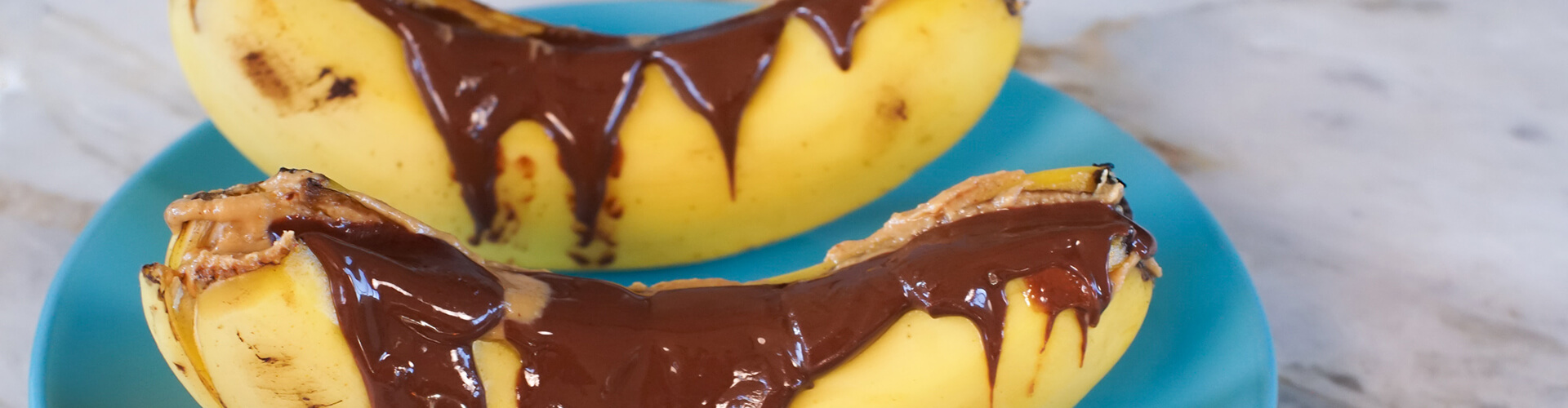 Duas banana split com pasta de amendoim e chocolift em um prato azul.