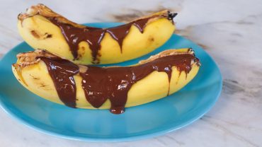 Duas banana split com pasta de amendoim e chocolift em um prato azul.