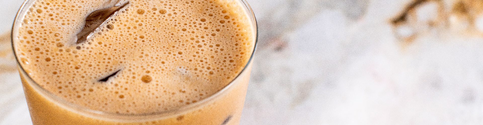 Um copo de vidro com café proteico gelado, em cima de uma bancada de mármore.