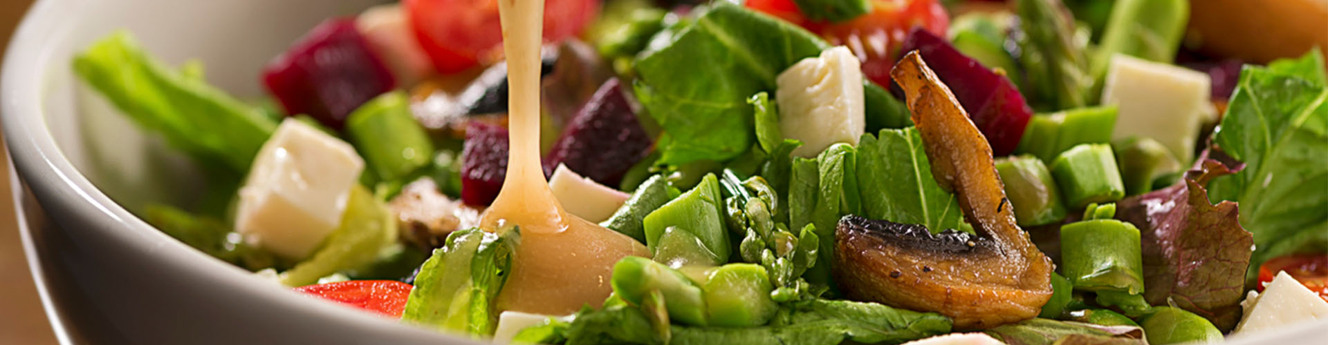 Molho de manga para salada sendo derramado em um mix de folhas e outros legumes