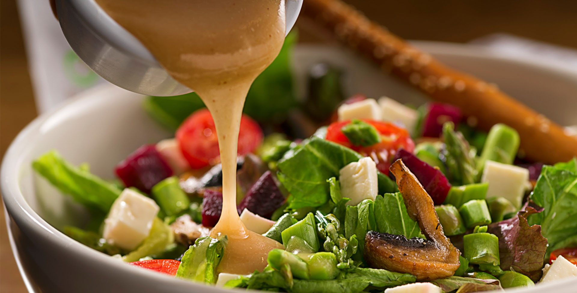 Molho de manga para salada sendo derramado em um mix de folhas e outros legumes