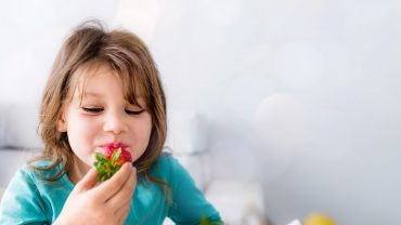 Criança com camiseta azul comendo um morango da sua alimentação saudável na infância