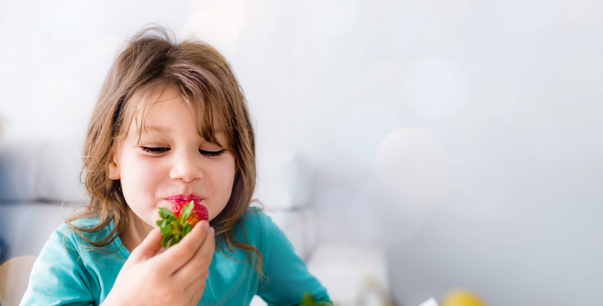 Criança com camiseta azul comendo um morango da sua alimentação saudável na infância