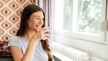 Jovem mulher bebendo água em frente à janela