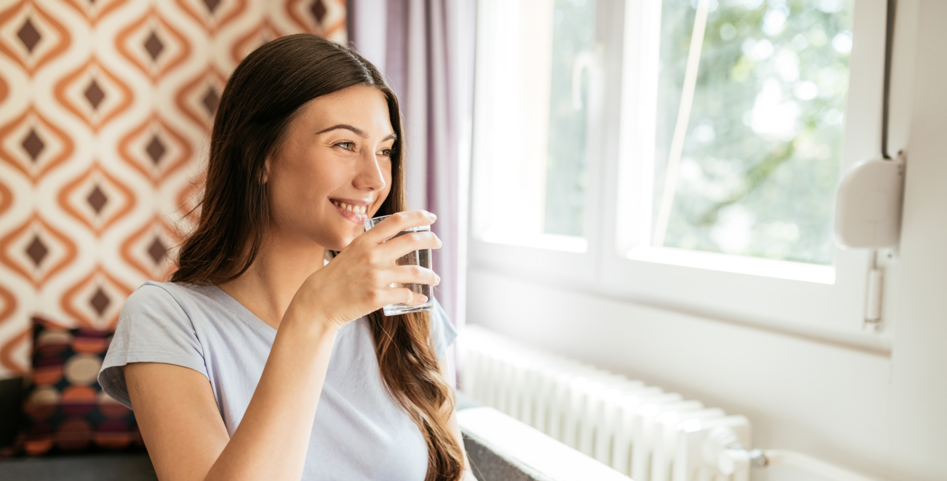 Jovem mulher bebendo água em frente à janela