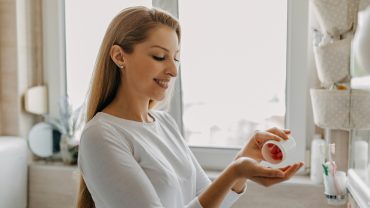 Mulher sorridente pega cápsulas de vitamina em um pote.