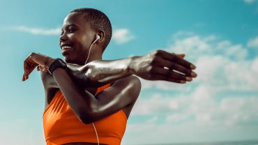 Mulher com top laranja se alongando para favorecer a recuperação muscular