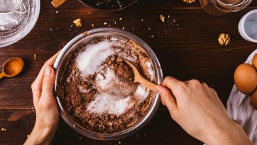 tigela com ingredientes vista de cima. A imagem mostra as mãos de uma pessoa. Uma segura a tigela e a outra mistura os ingredientes com uma colher de madeira