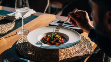 Homem utilizando garfo para comer um prato sofisticado em restaurante bem iluminado, ilustrando a relação entre GLP-1 e falta de apetite.