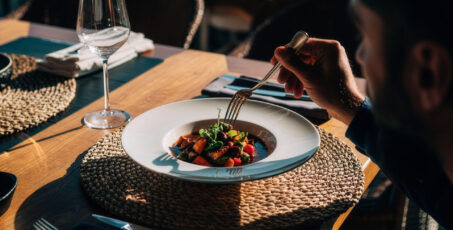 Homem utilizando garfo para comer um prato sofisticado em restaurante bem iluminado, ilustrando a relação entre GLP-1 e falta de apetite.