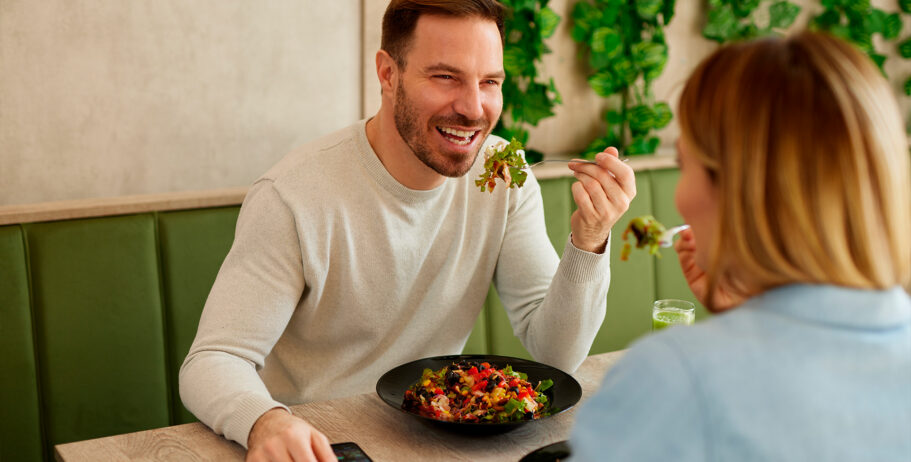 Homem e mulher compartilham uma refeição saudável com salada colorida em um ambiente agradável. Uma alimentação equilibrada, rica em proteínas, fibras e gorduras saudáveis, pode ajudar a estimular a liberação natural de GLP-1 e favorecer a saciedade